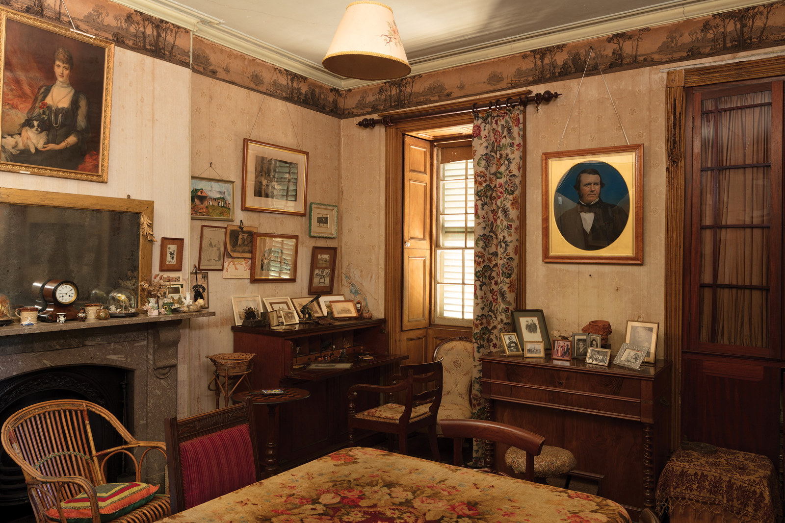 Corner of room with harmonium and several framed photographs near window.