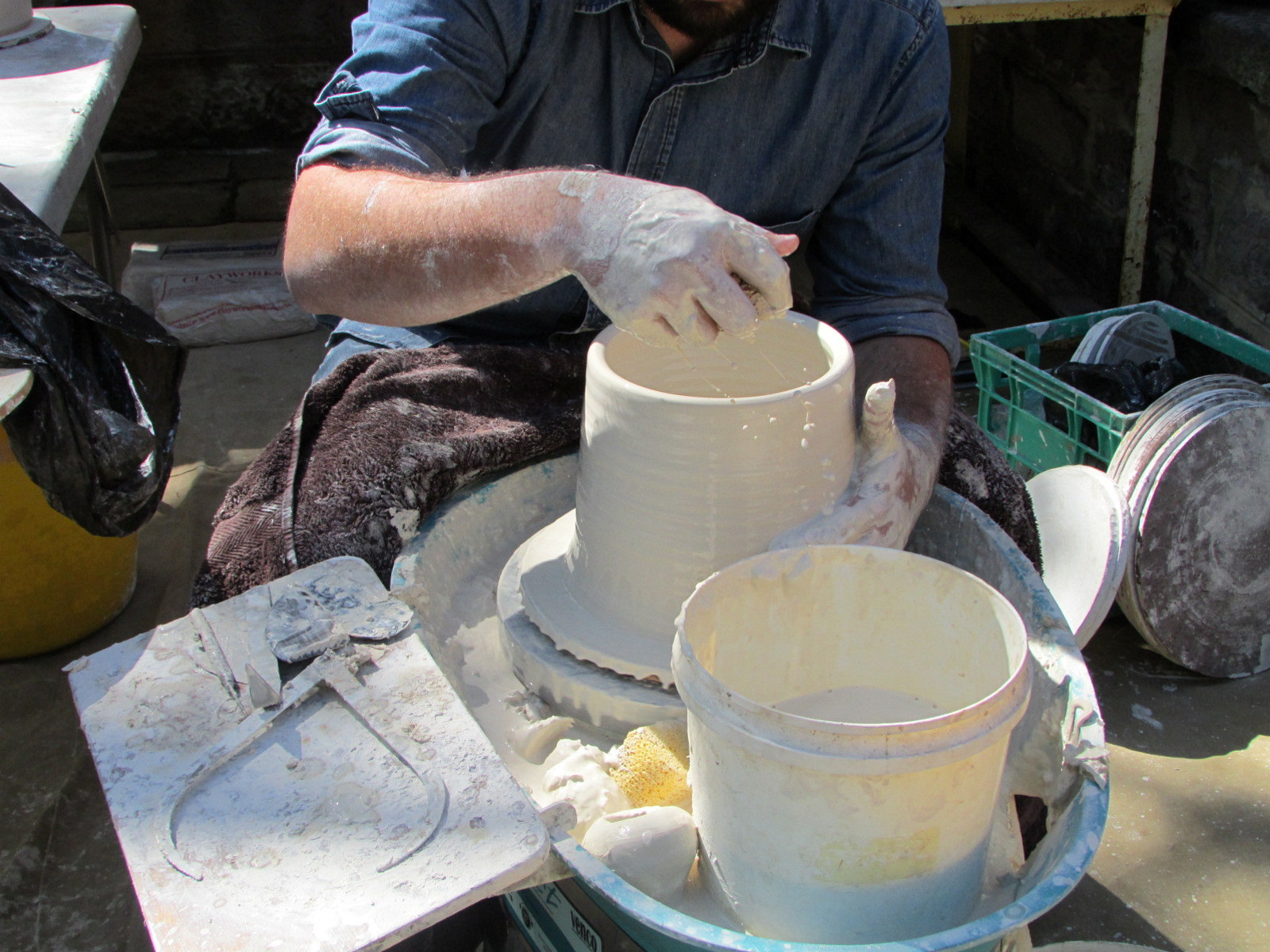 a white cylindrical ceramic vessel on a potter's wheel is almost complete