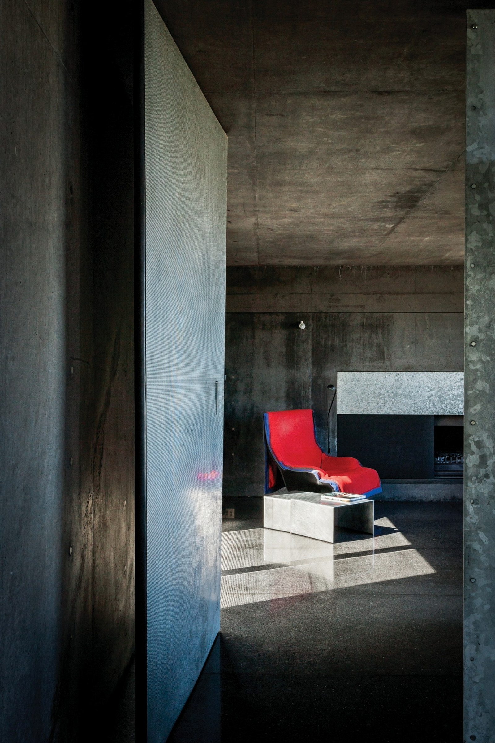 This is a photograph taken from outside the doorway to a concrete room with a bright red chair in the centre