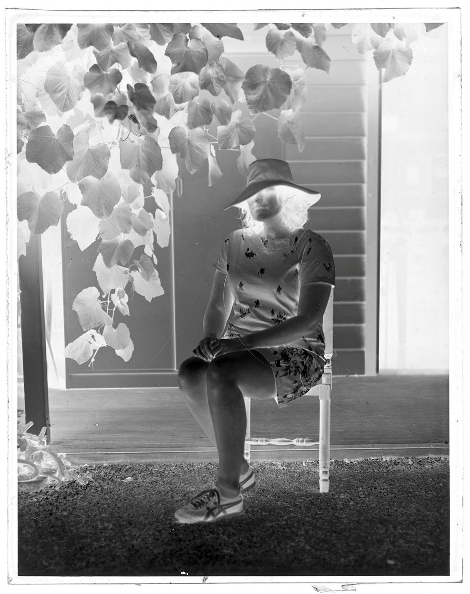 Black and white negative of woman sitting on chair in garden.