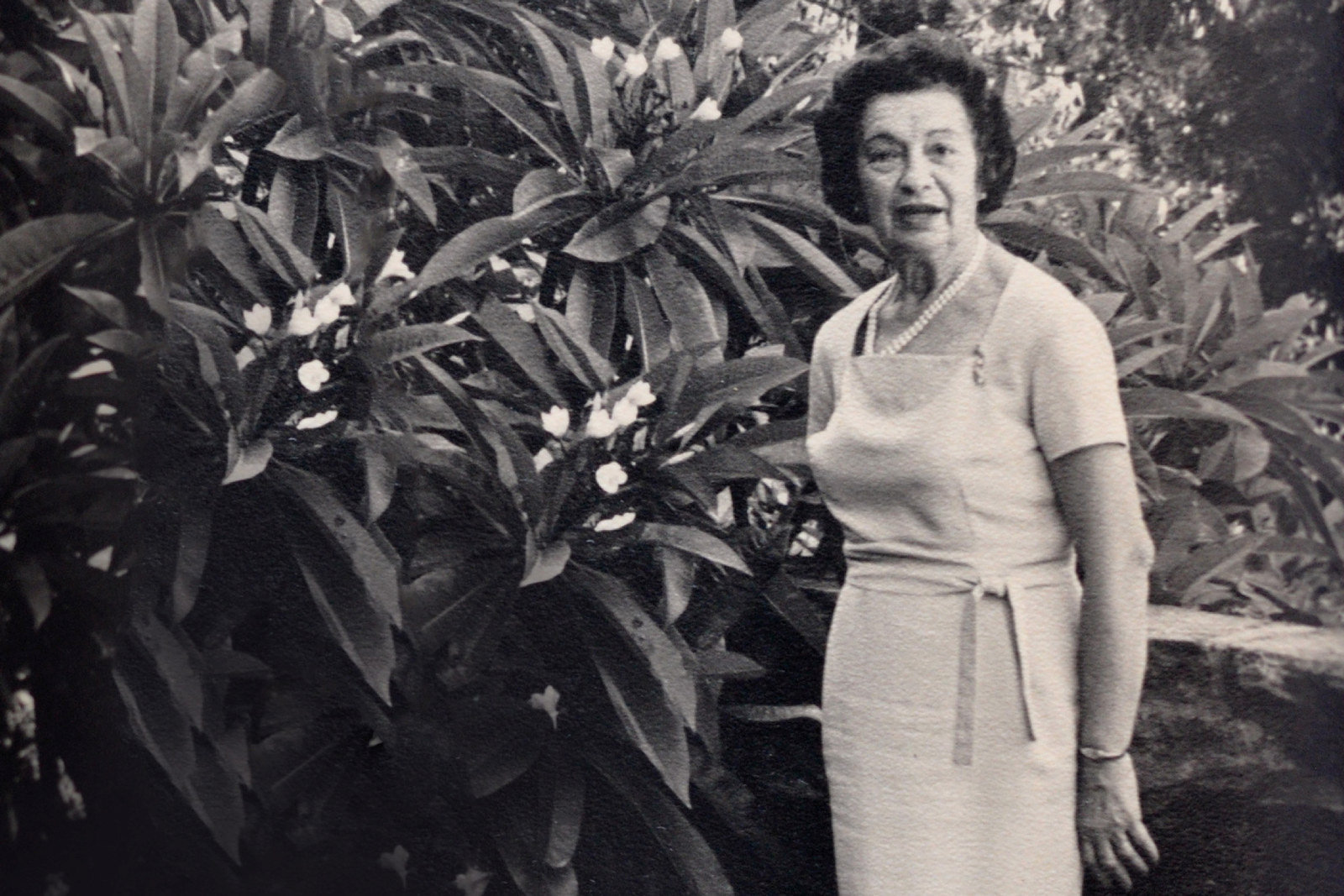 Black and white image of woman standing in front of bush in garden.