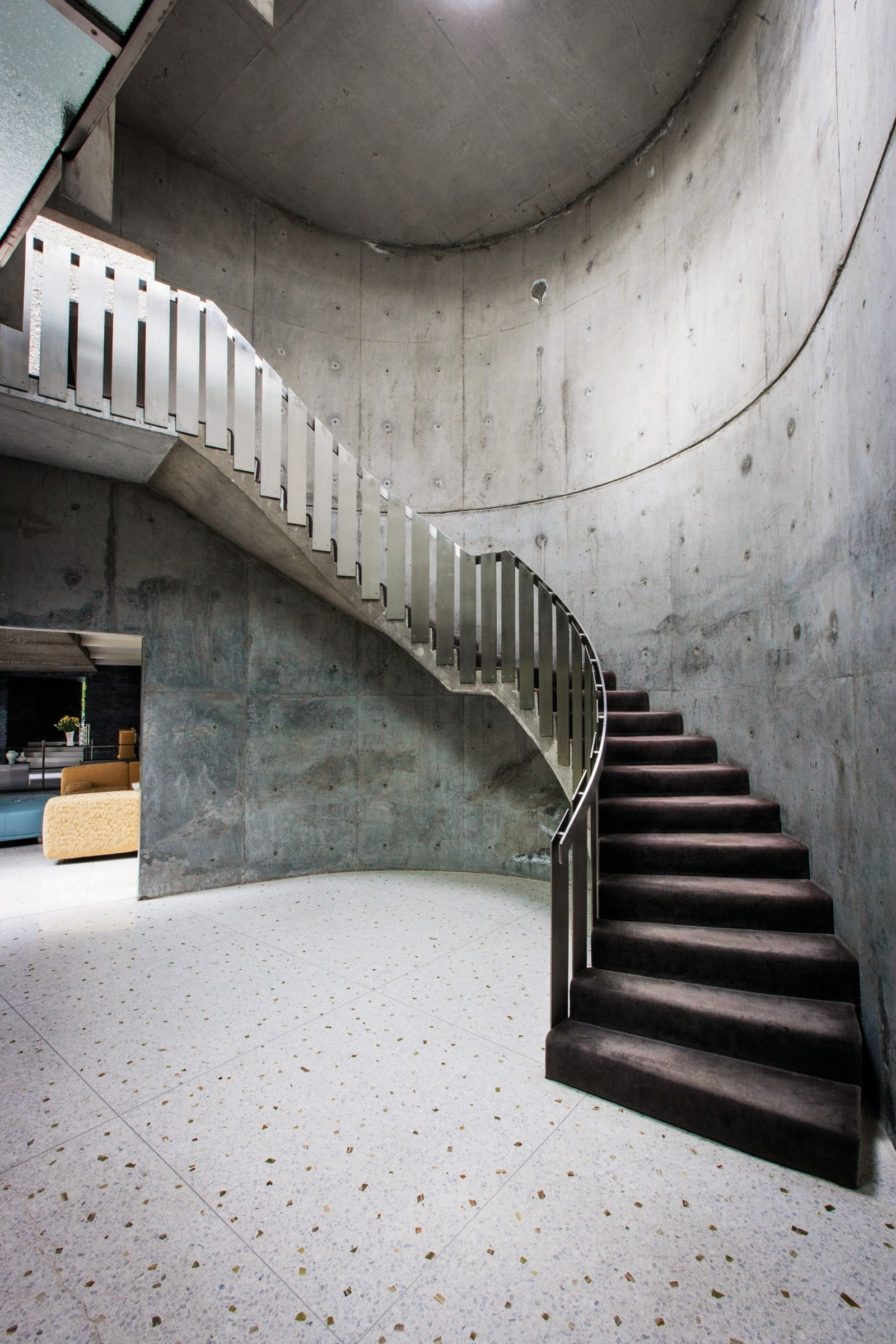 This is a photograph of an atrium with concrete walls and floor and a large sweeping concrete staircase with metal balustrade