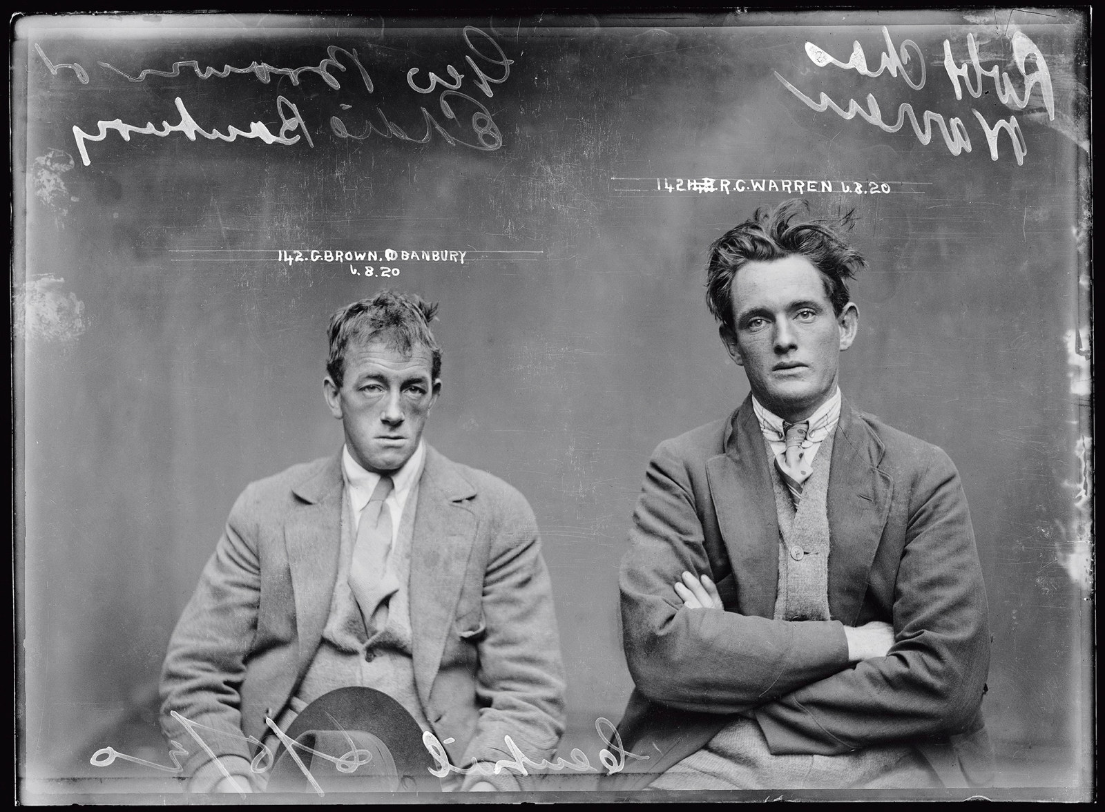 Black and white mugshot of two seated men.
