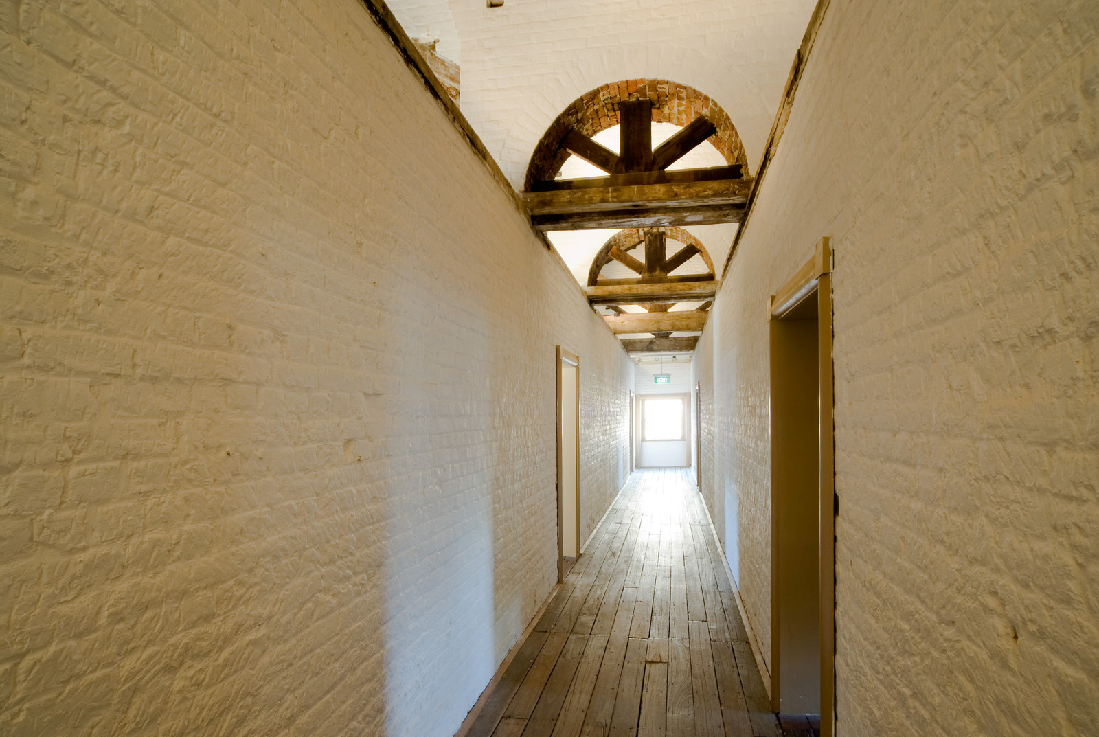 View along interior corridor towards sunlit window, with wooden ceiling arches visible.