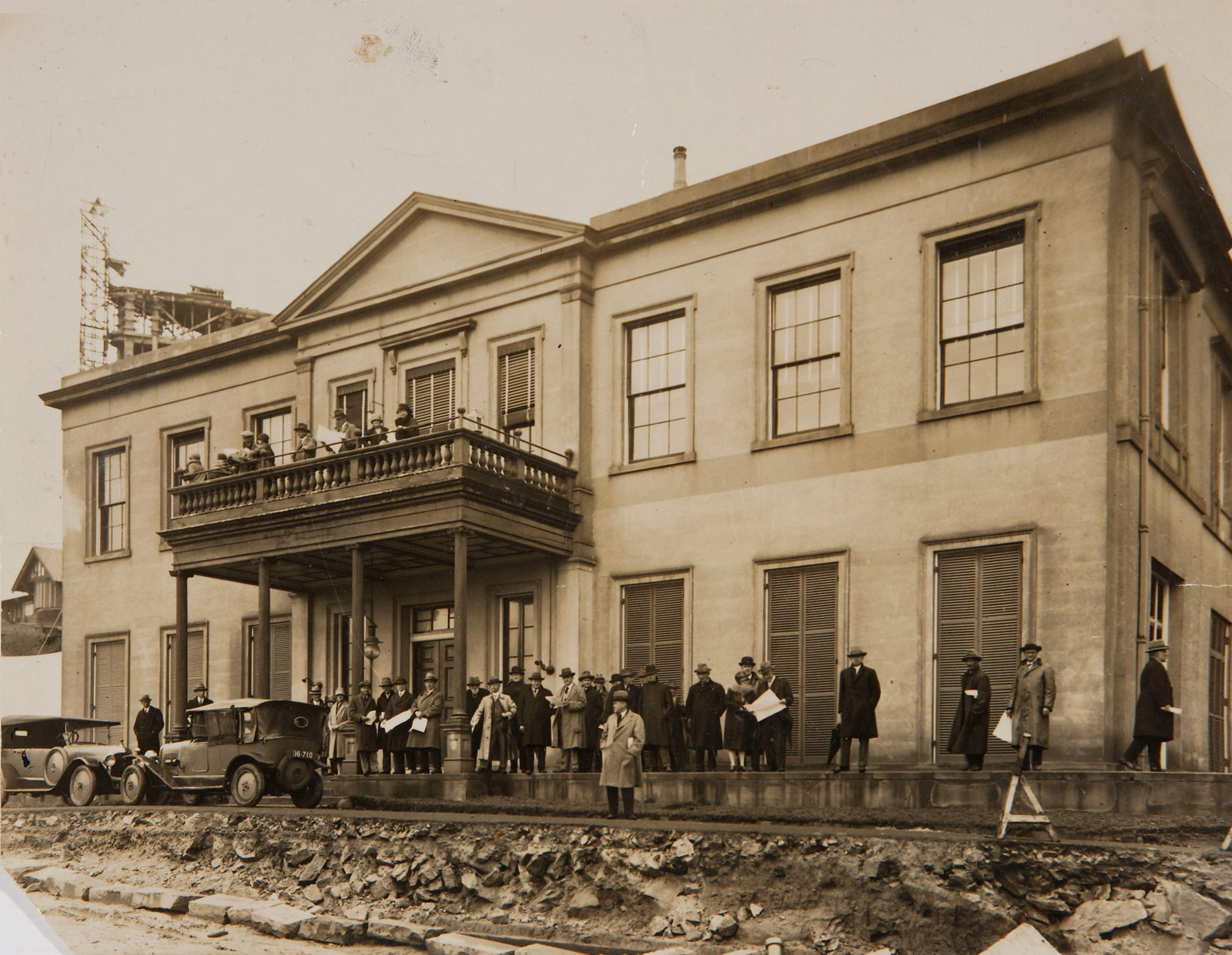 B/w photo of a large group of people standing in front of Elizabeth Bay House, with roadworks underway in front of the building.