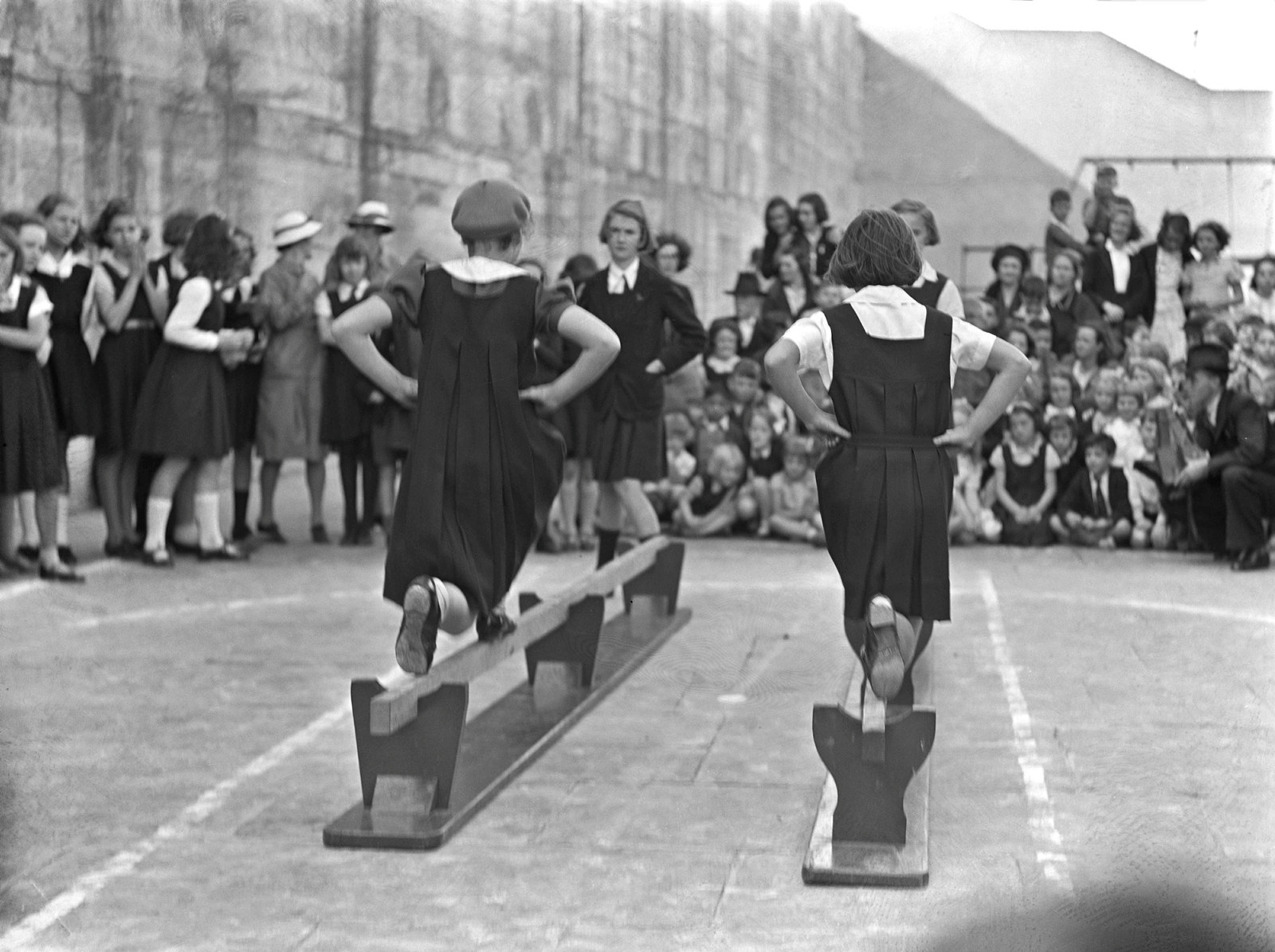 Black and white photo of children in black tunics doing exercises.