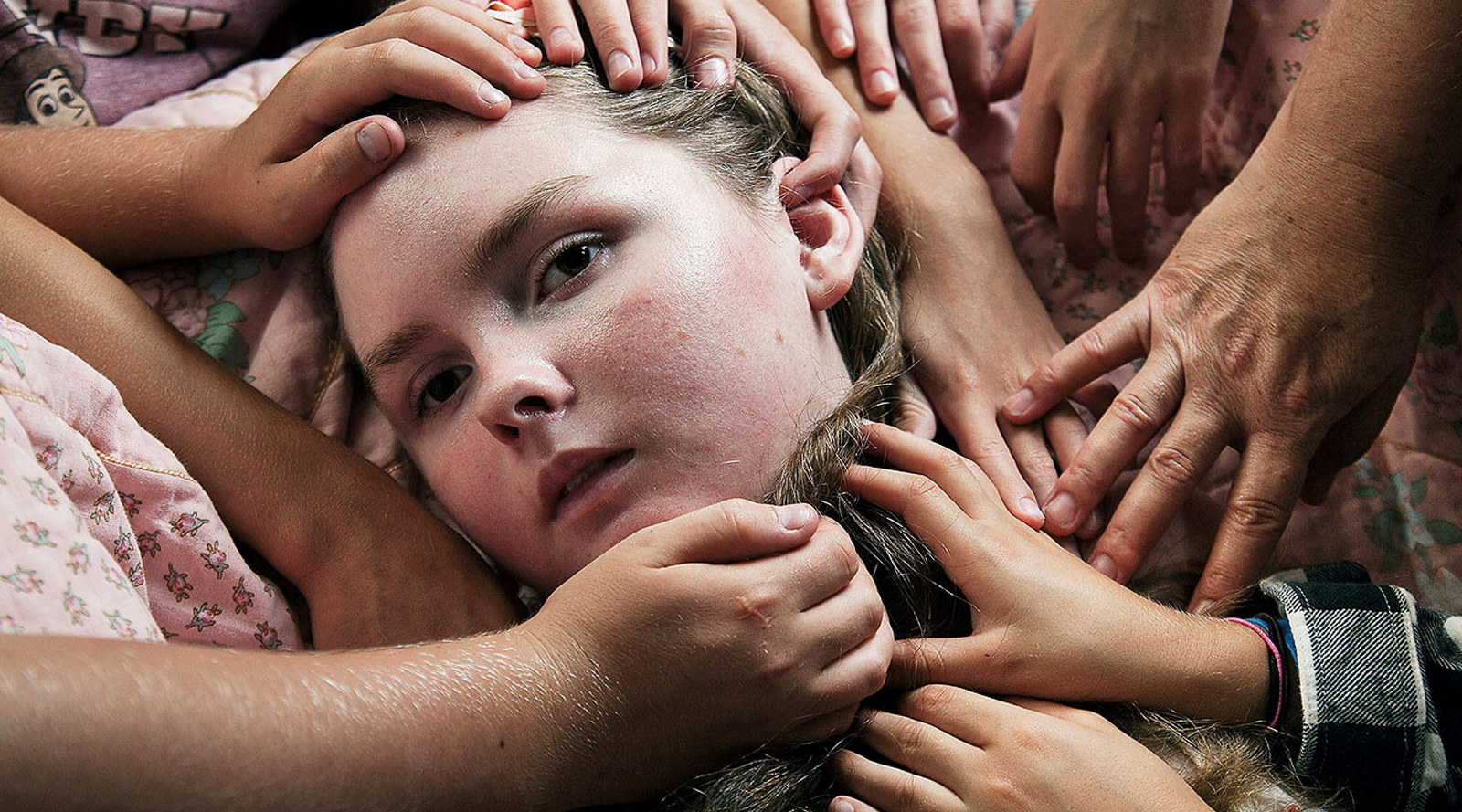Closeup of girl's face with many hands holding or framing it.