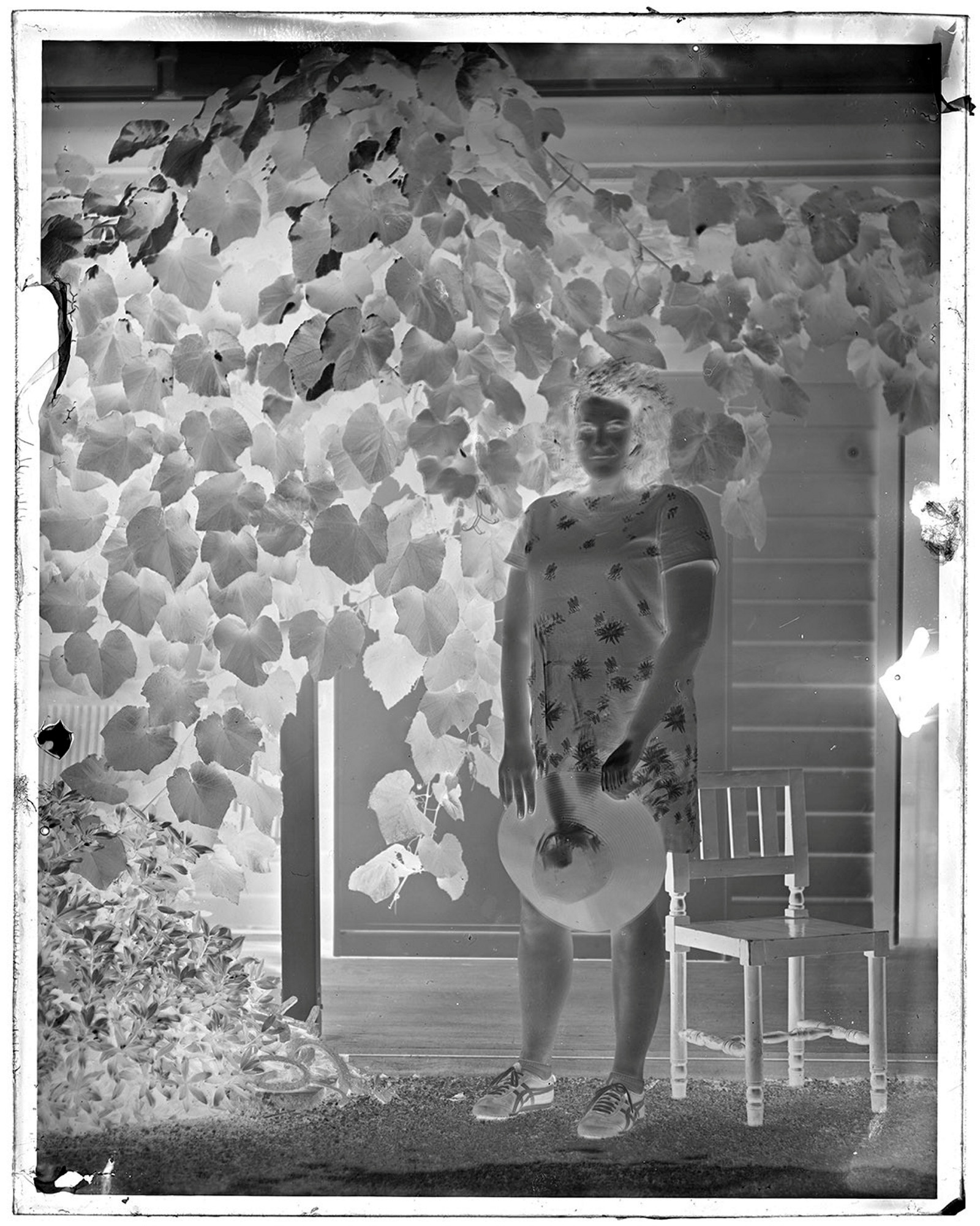 Black and white negative of woman standing in garden.