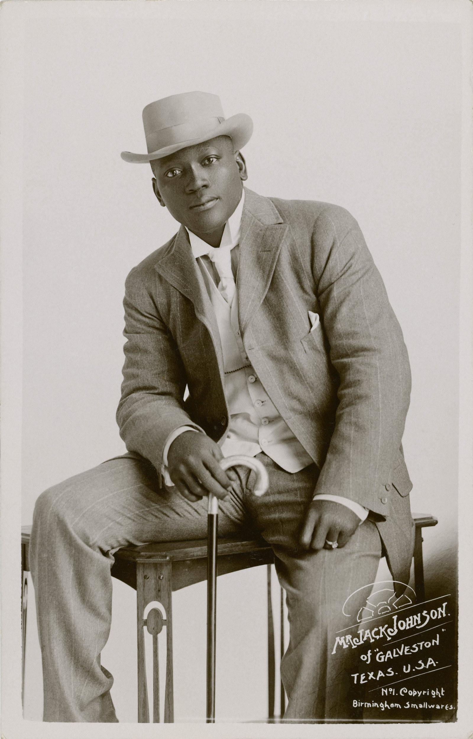 Boxer Johnson sits on a table wearing a brown suit and hat, holding a cane.