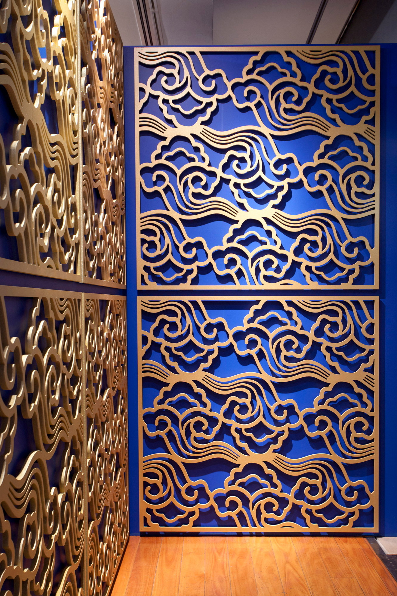 This is a photograph of gold painted cut-out panels featuring a cloud pattern on a blue wall