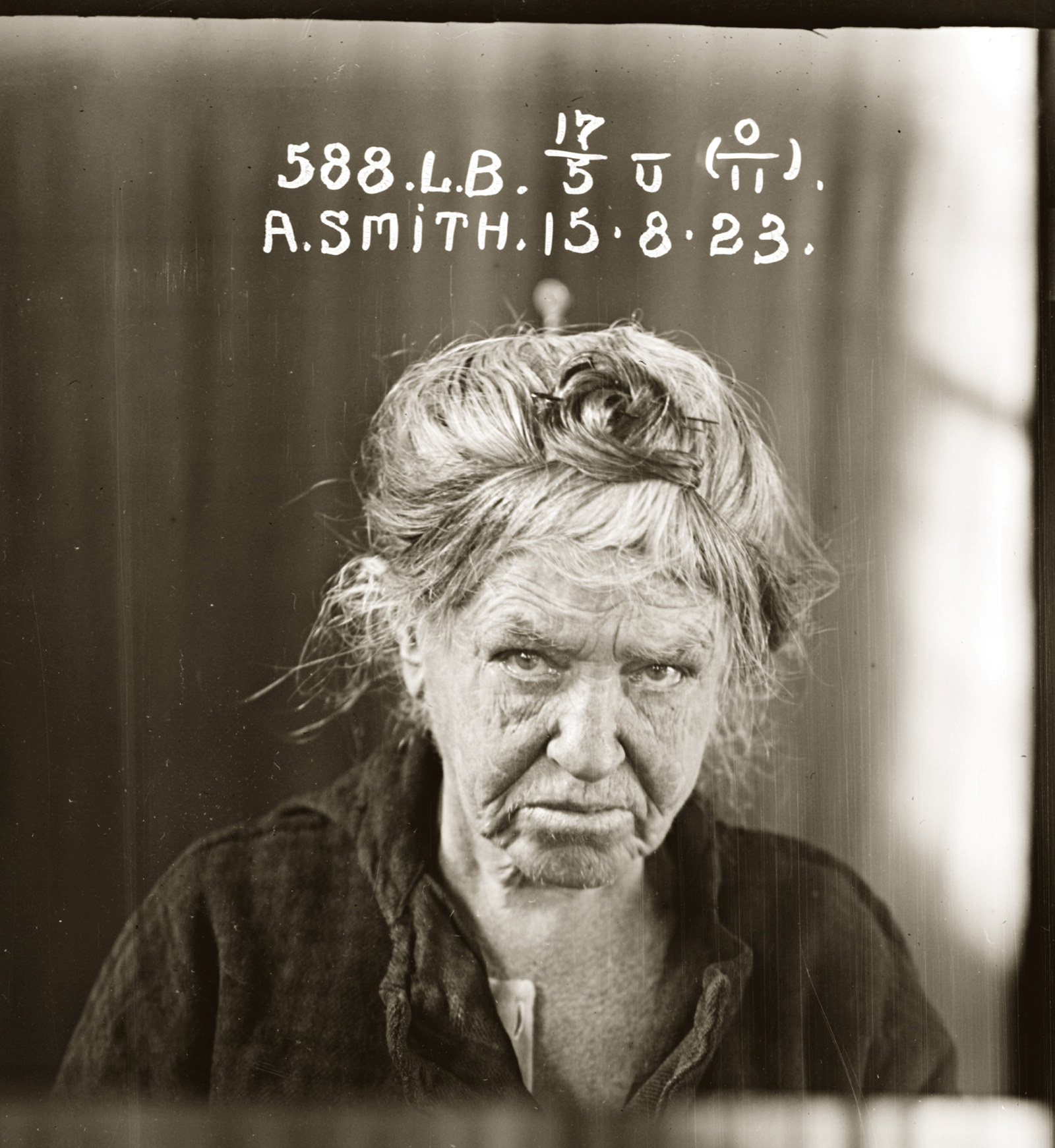 Black and white photo of older woman with white hair piled up on head, looking downcast. Image hand-inscribed with woman's details and date.