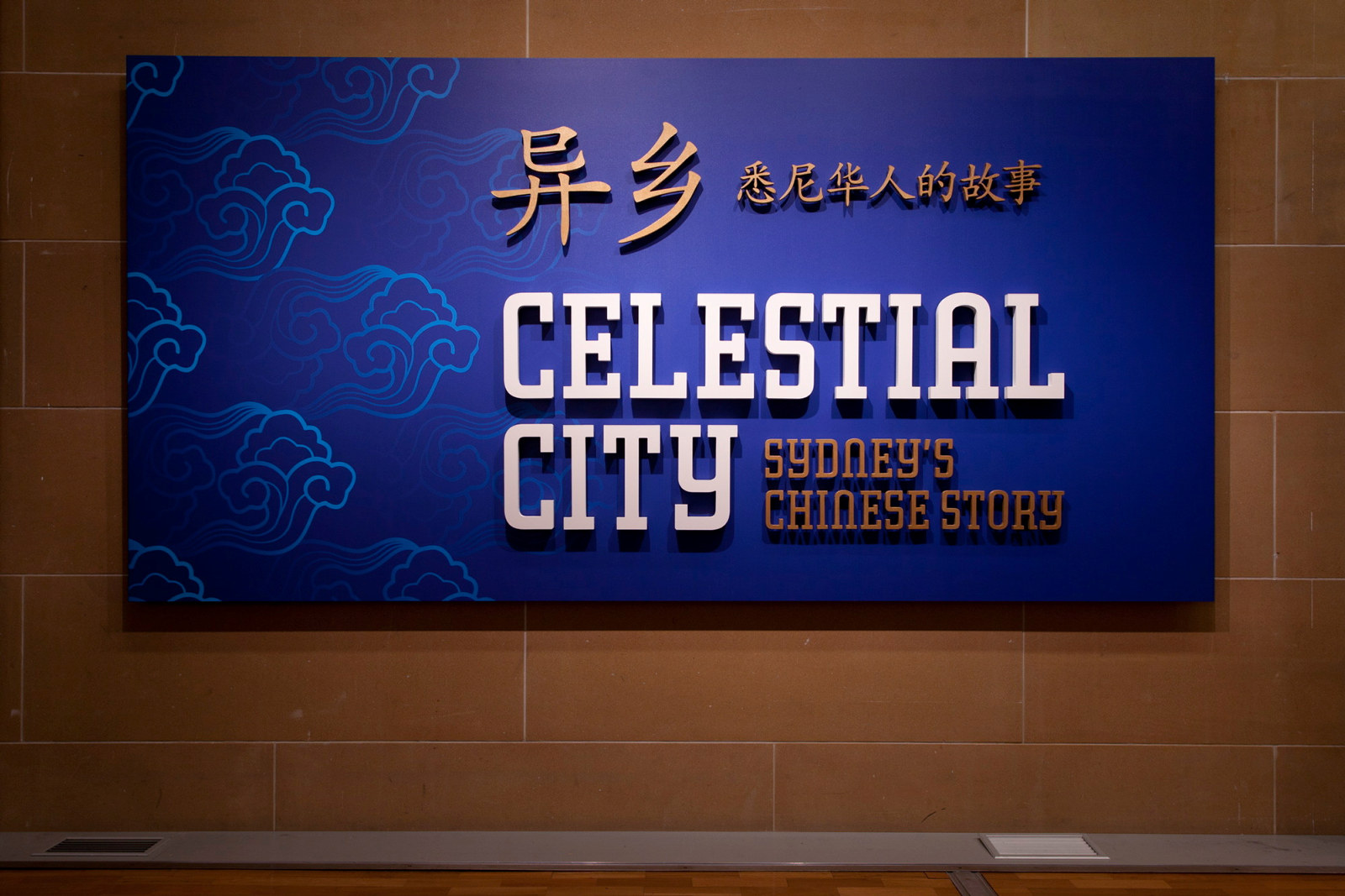 This is a photograph of a blue panel on a sandstone wall. On the panel in white lettering are the words Celestial City with gold lettering for the words Sydney's Chinese Story and the Chinese language translation