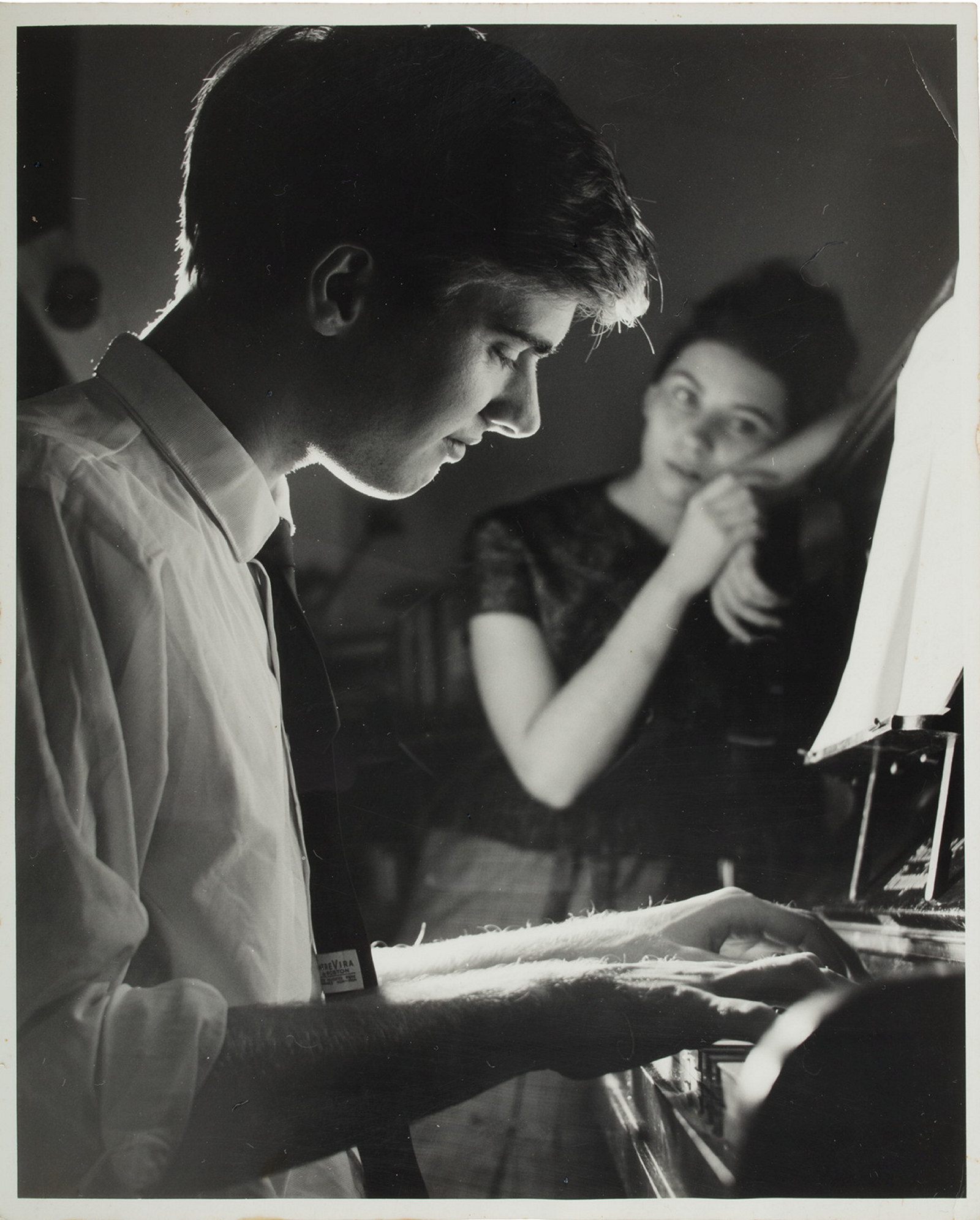 A black and white contemporary photograph of John Terry playing the piano. Caroline Terry (later Caroline Thornton) is shown in the background on right, leaning against the piano.