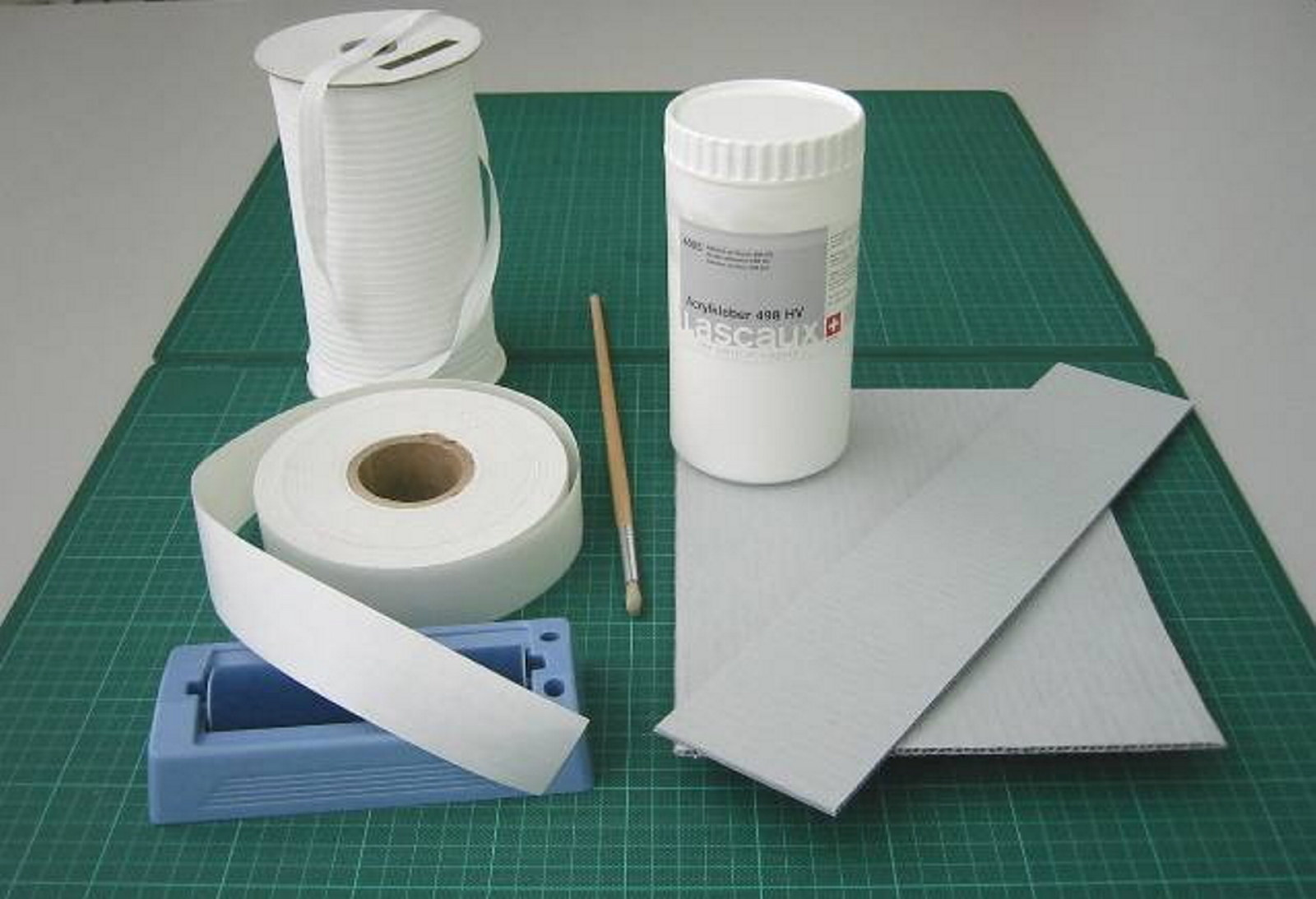 Fig. 3 - Materials clockwise from top left, cotton tape, Lascaux, corrugated board, gummed linen tape. Included are a roller damper for wetting the linen tape and a brush for applying the adhesive