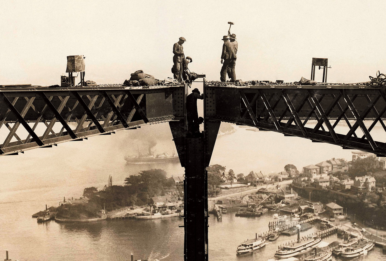 Image of a partly constructed bridge with workers standing on steel girders high above the harbour.