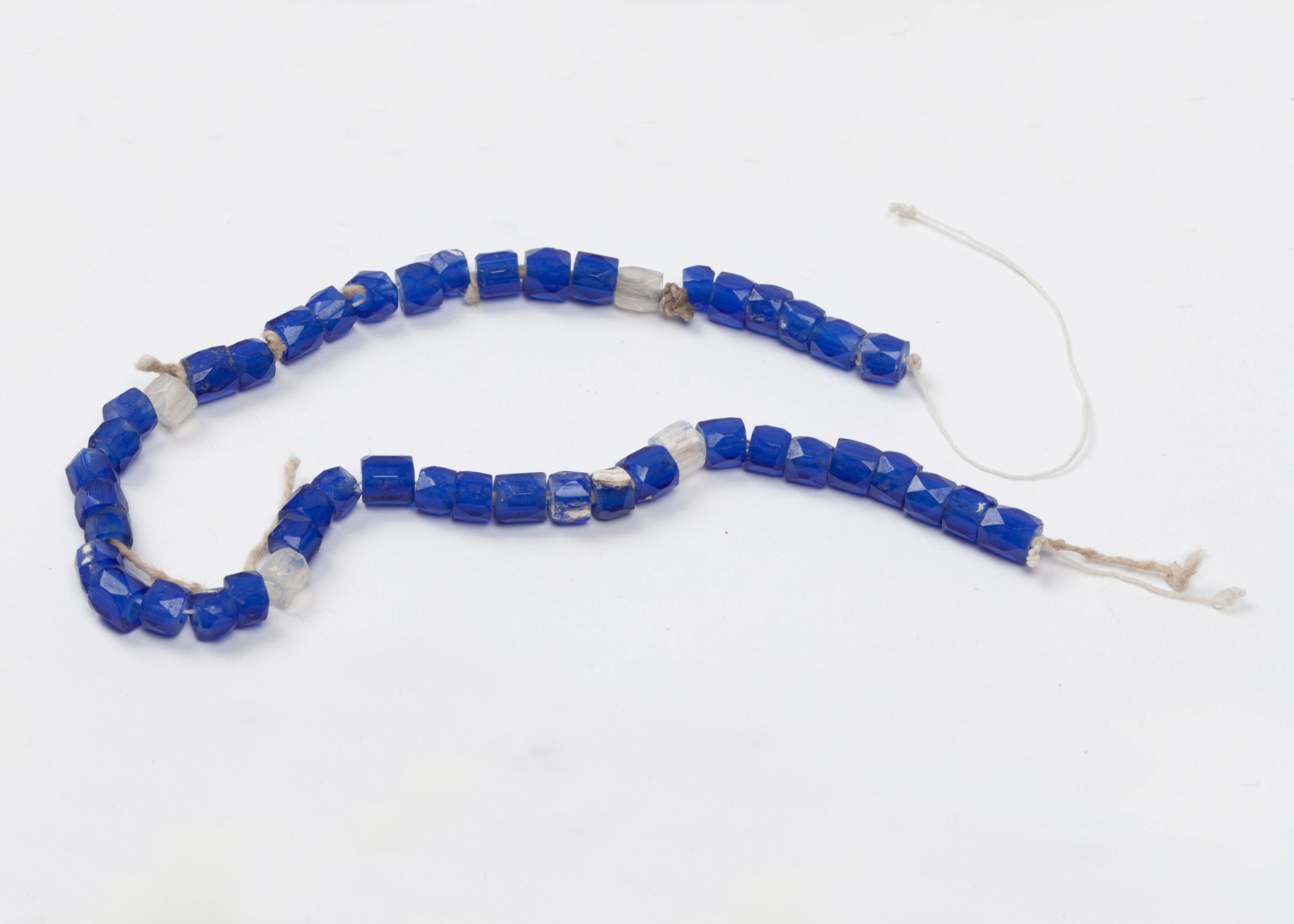 String of blue glass rosary beads, featuring mainly blue beads with the occasional white bead, connected with white string.