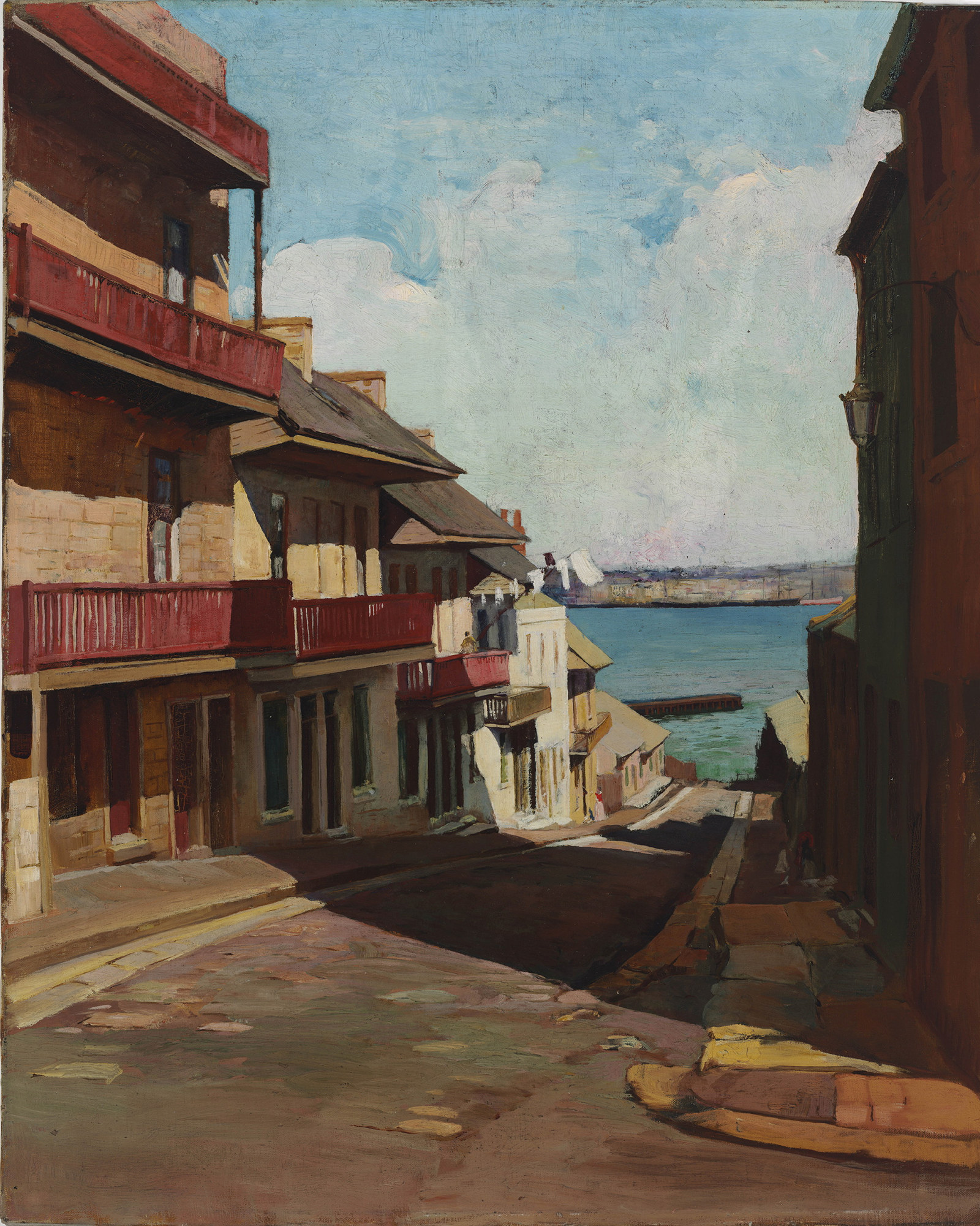 View down a steep narrow street lined with terrace houses of the blue water of the harbour at its end.