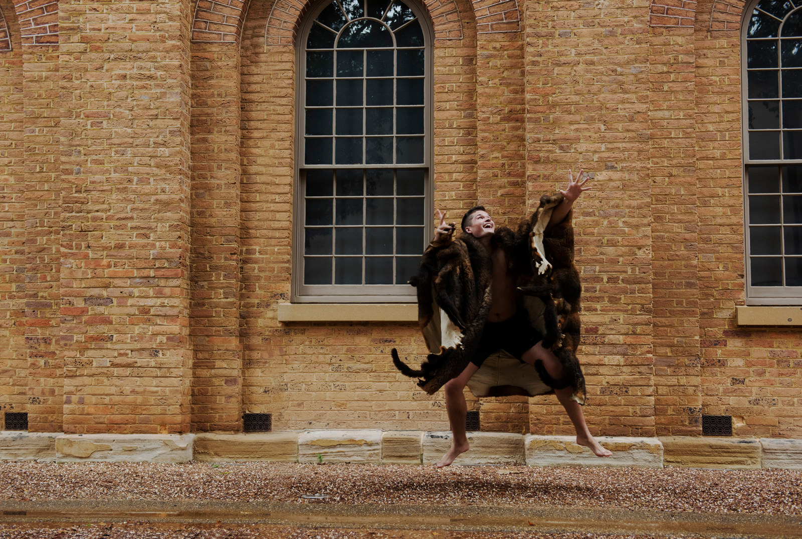 Campaign photos for Cutter and Coota, featuring a performer dressed in a possum skin cloak posing within the grounds of the Hyde Park Barracks.