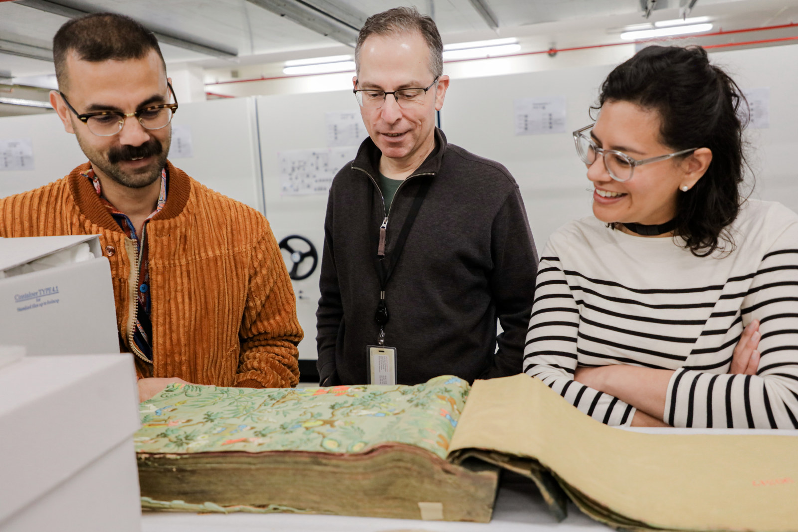 Aaron de Souza, Michael Lech and Julieanne Rabier view a wallpaper sample book from the John and Phyllis Murphy collection, Museums Discovery Centre