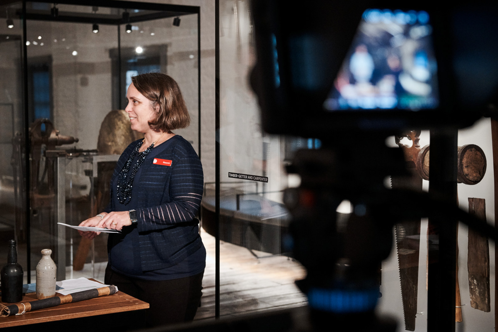 Naomi Manning, Producer – Learning Programs, stands in front of a series of cameras as she presents a virtual excursion. She is standing behind a table of historical objects in the Meet the Convicts room on the top floor of the Hyde Park Barracks.