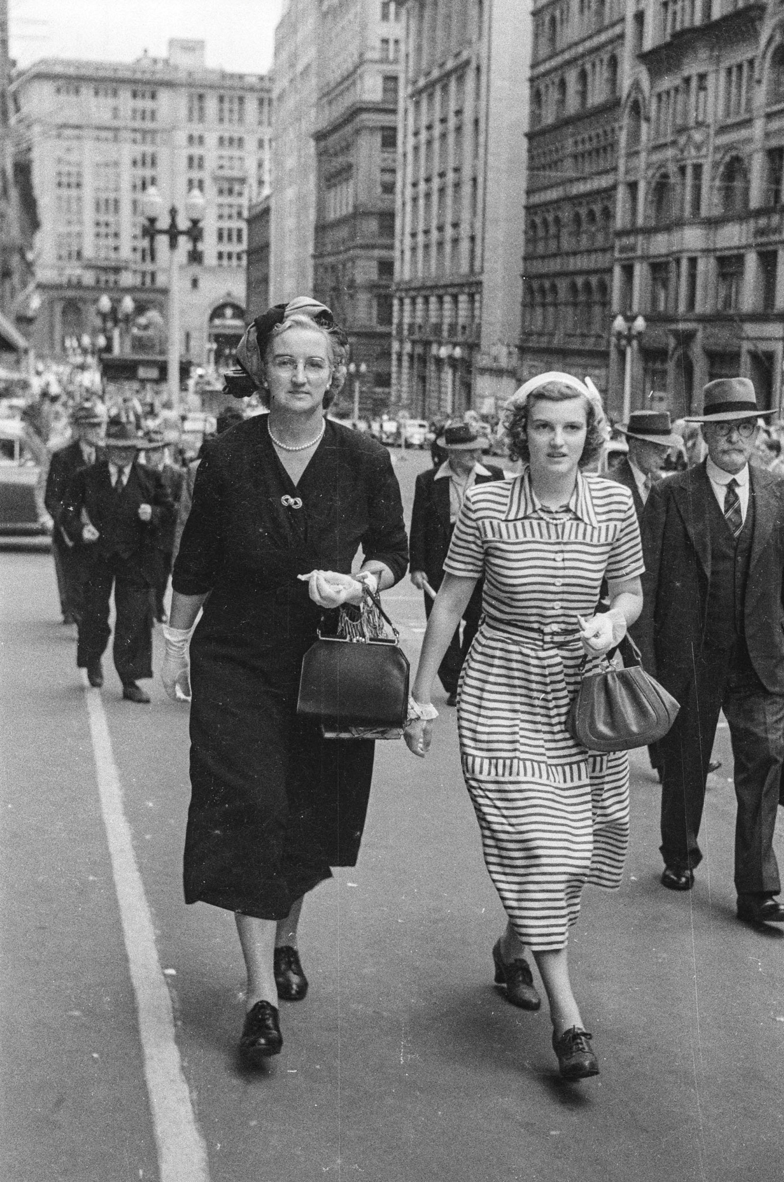 Black & white candid photo of people walking down city street.