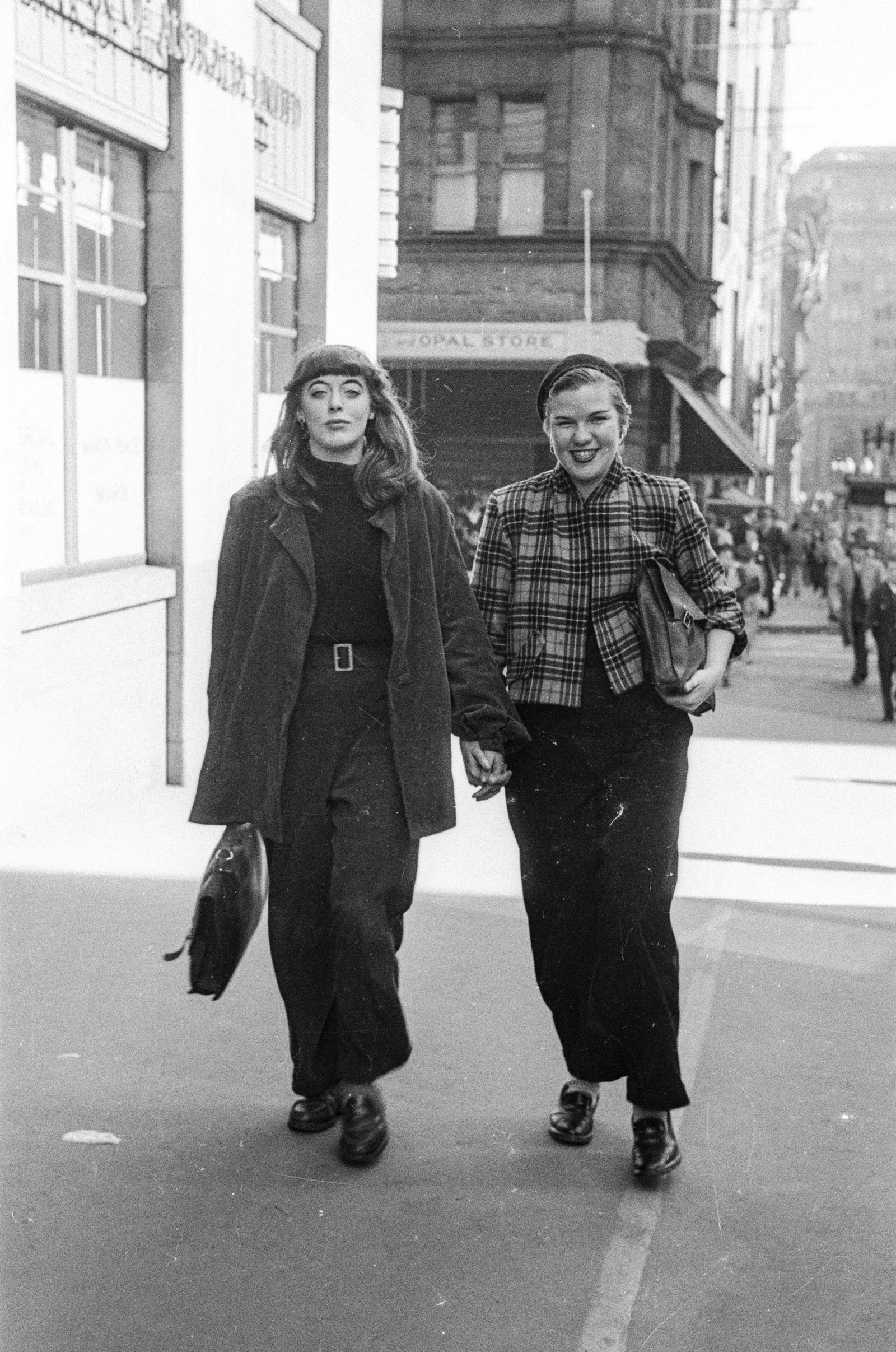 Black & white candid photo of people walking down city street.